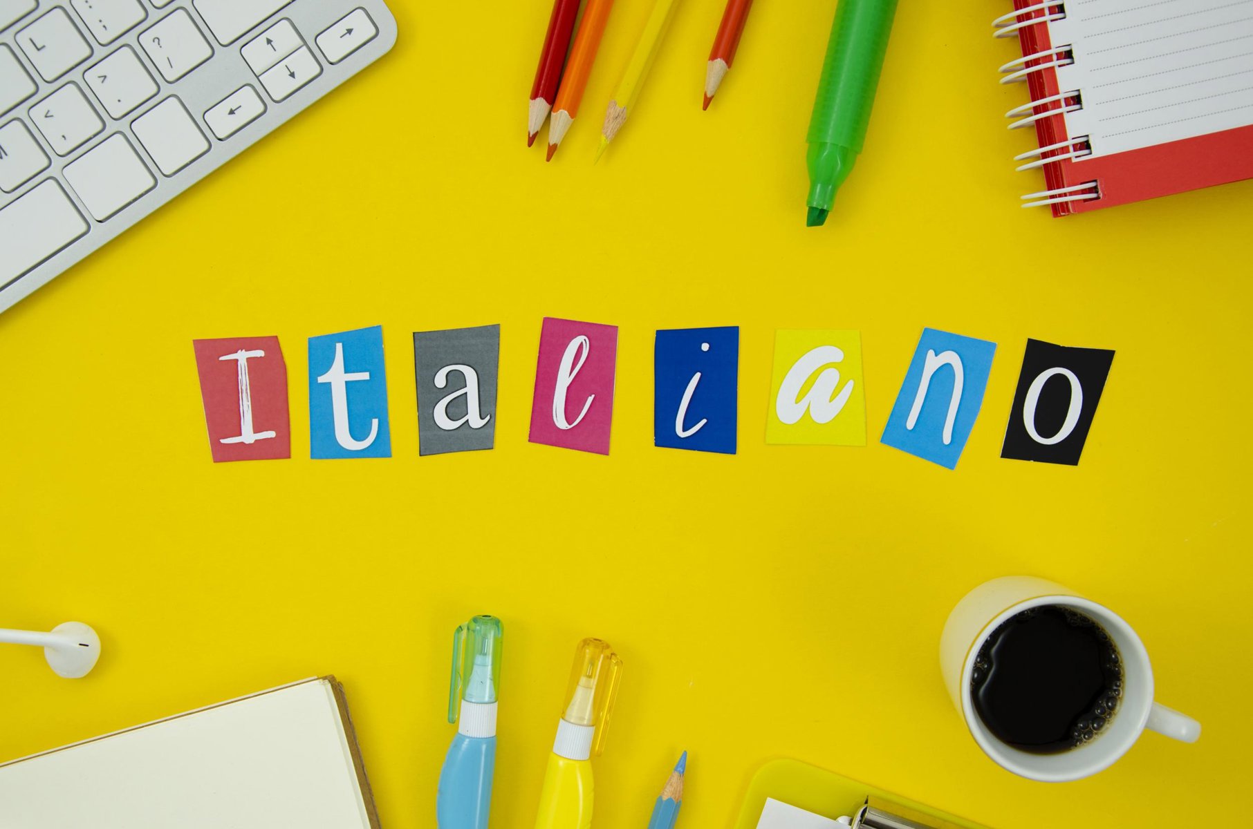 Italienisch-Wort aus ausgeschnittenen Buchstaben auf gelbem Untergrund mit Büromaterialien